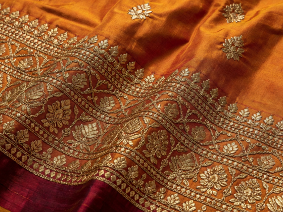 Intricate golden zari work on deep saffron-maroon pure Banarasi silk fabric